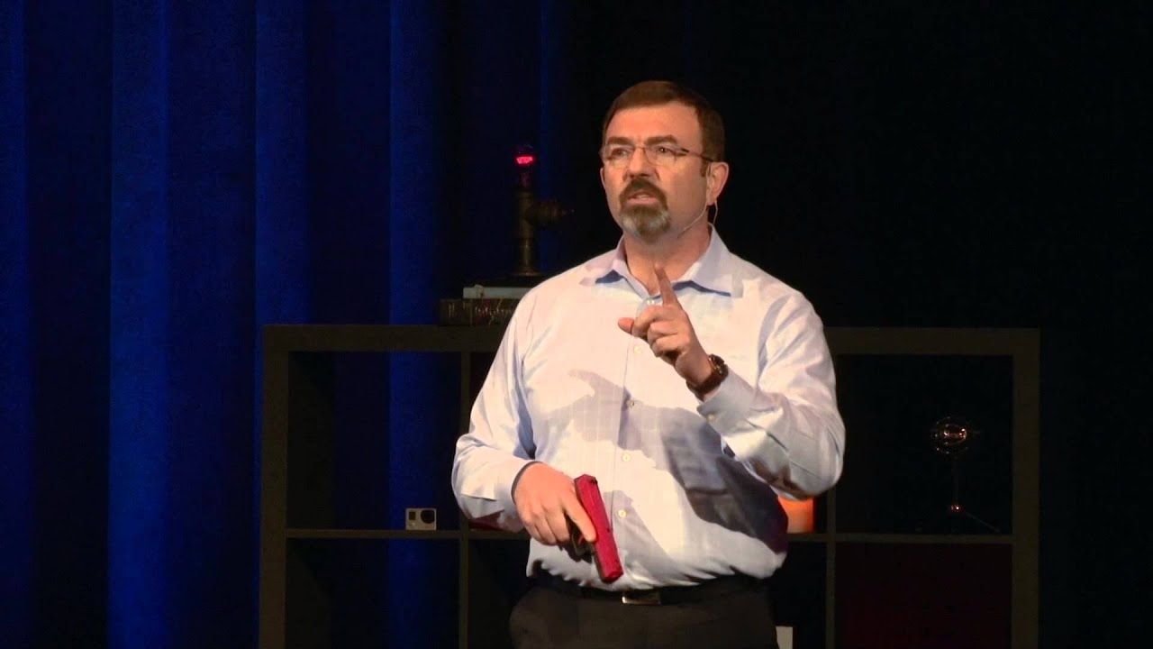 Brian Willis A police instructor speaks on stage holding a training firearm