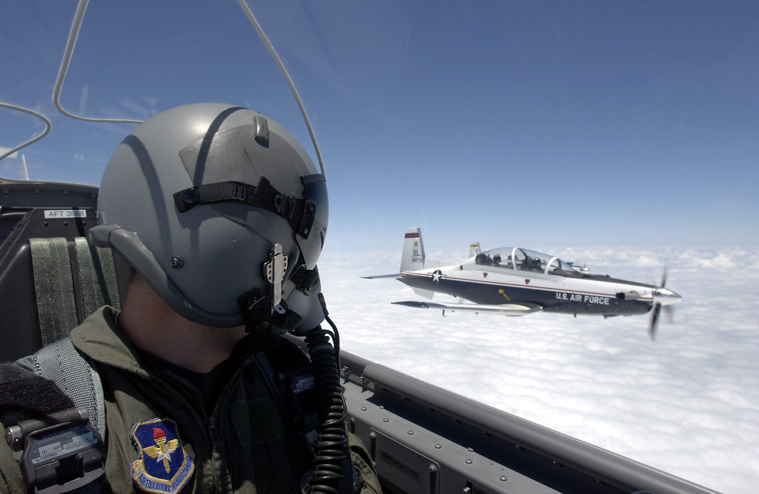 Air Force Pilot in helmet and oxygen mask looks from his plane to a plane just off of his left wing. 