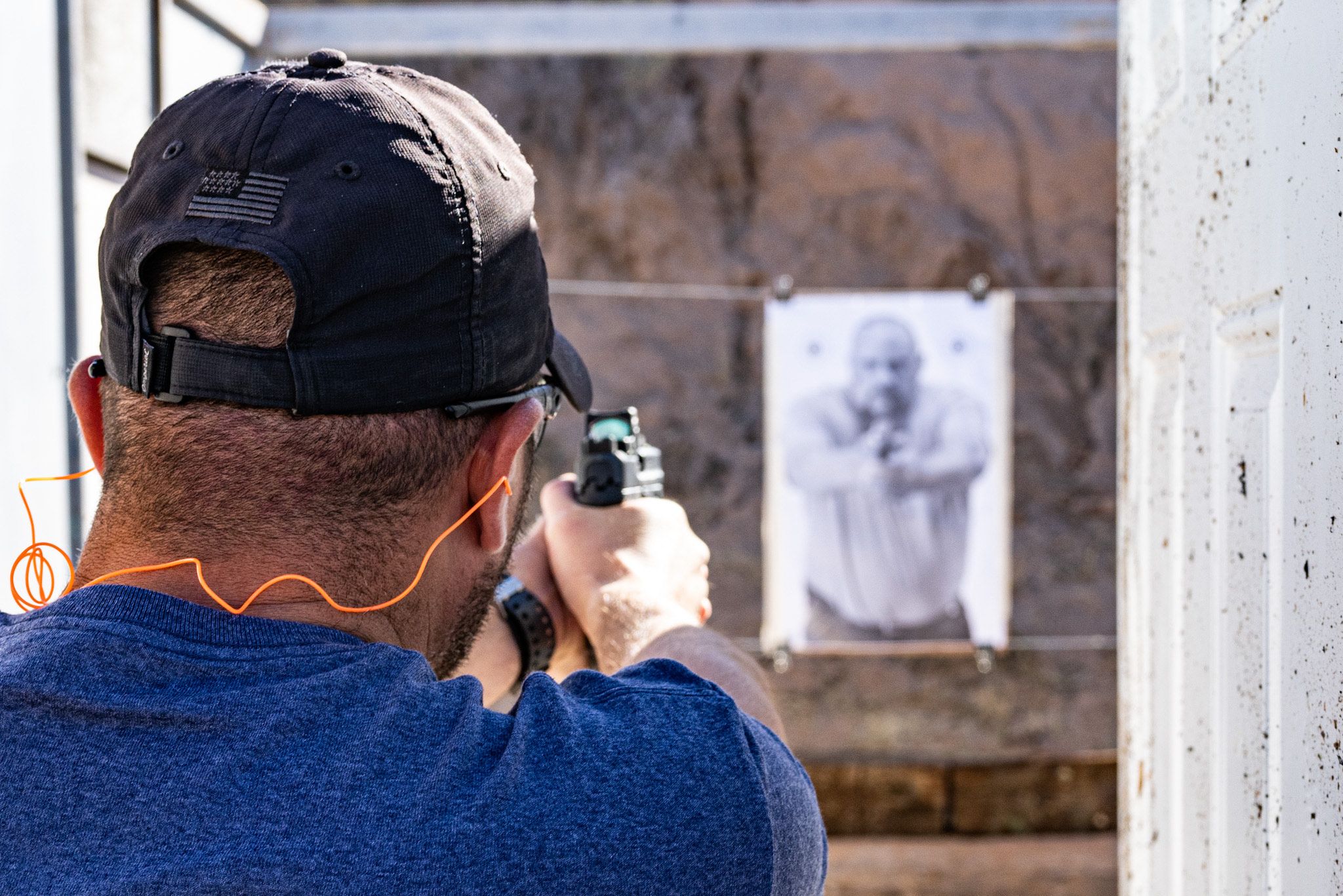 Male practicing shooting techniques on a range, using a pistol with a pistol mounted optic. 