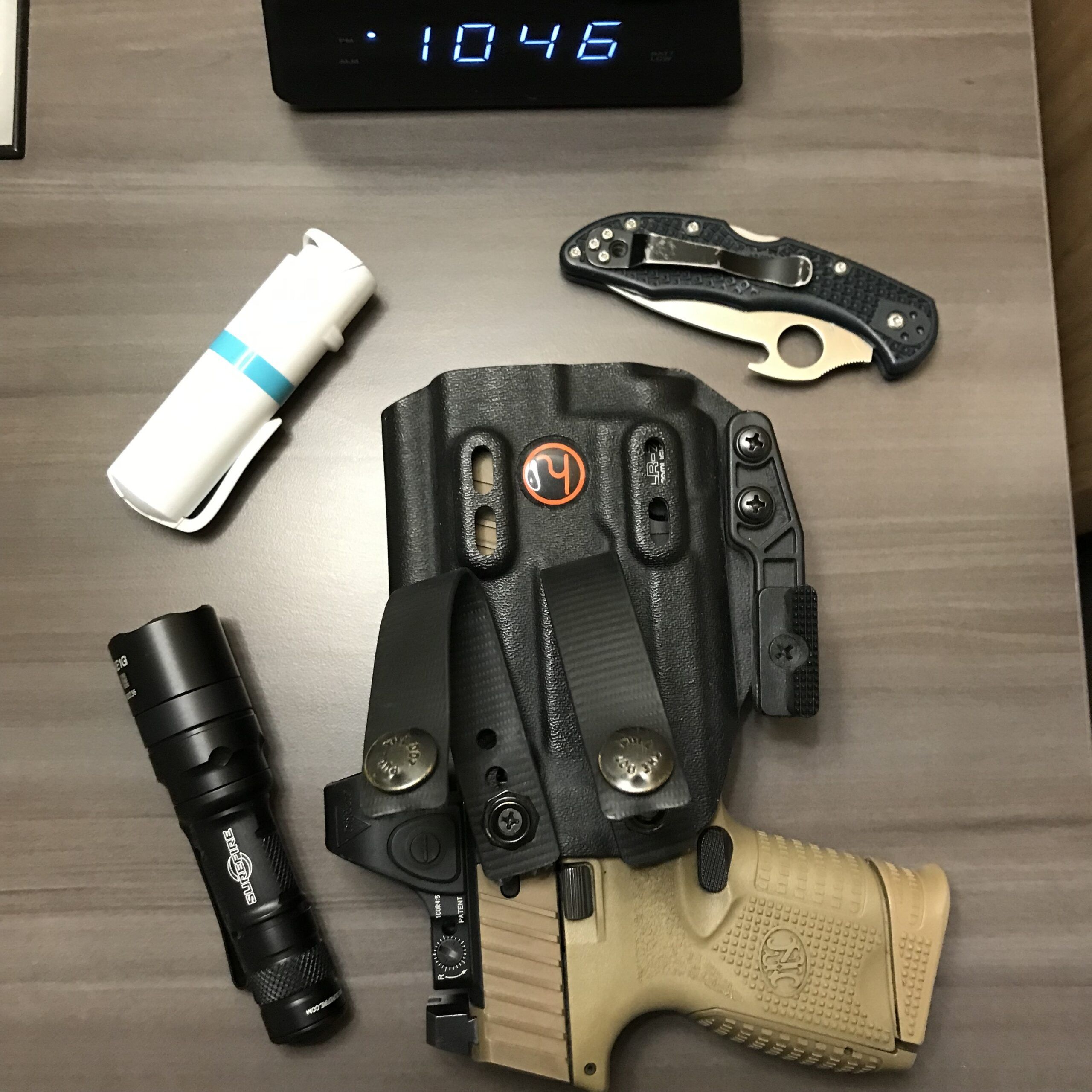 A flat layout of some everyday carry tools, including a firearm, knife, flashlight, and pepperspray