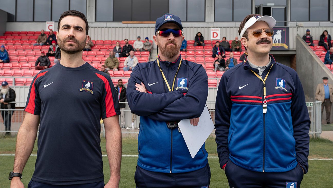 three inspirational TV coaches posed on the football pitch looking at their players practice