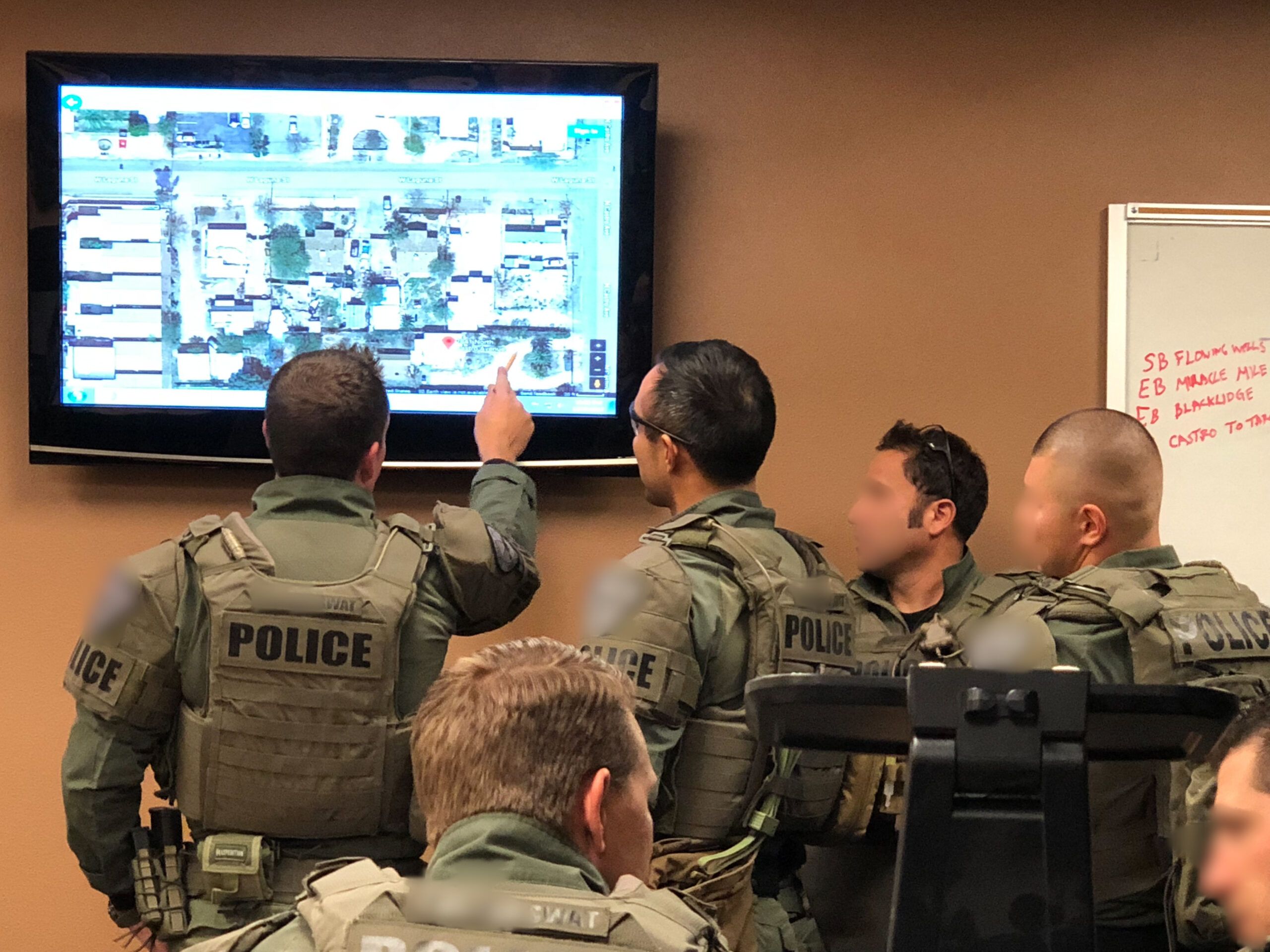 Police SWAT operators planning over a digital map on a television mounted on the wall