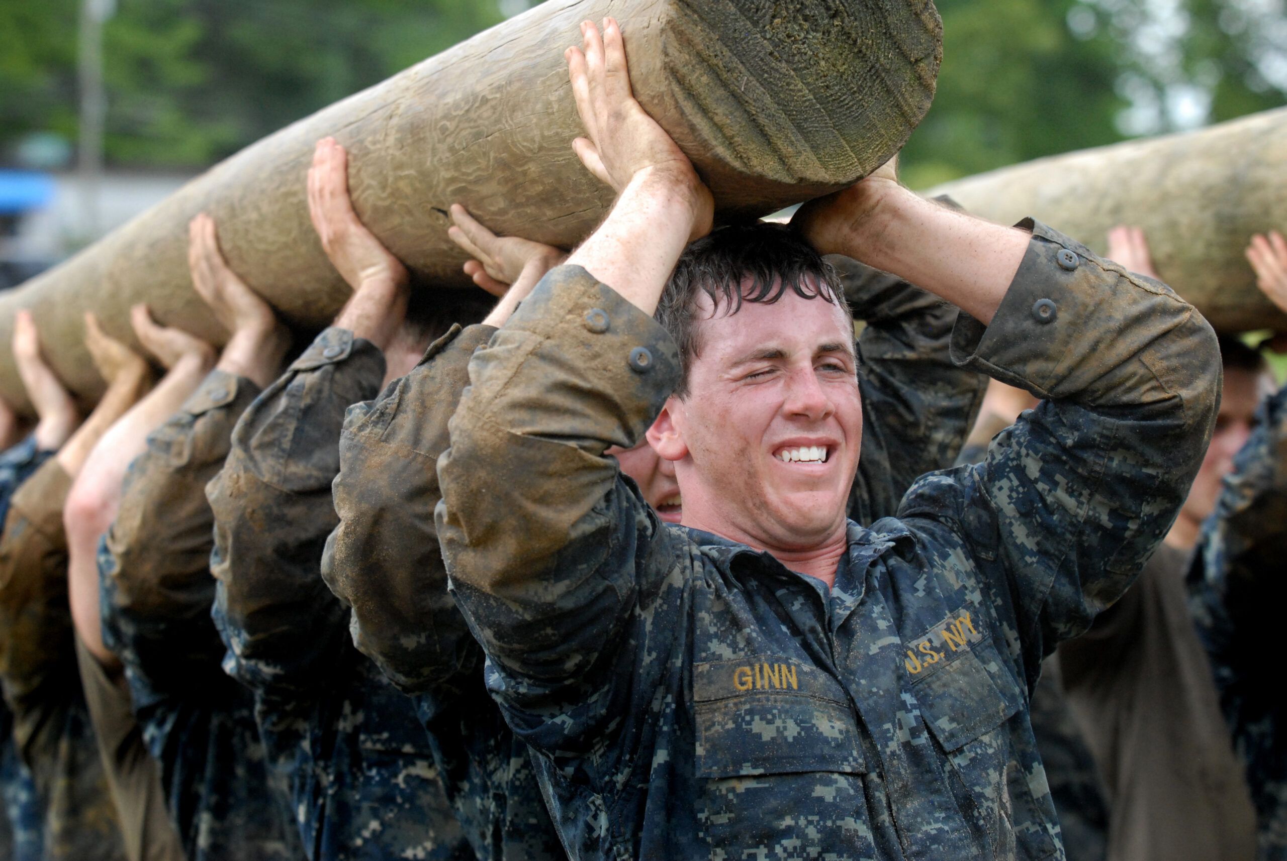 team of military members lifting a log over their heads as one unit