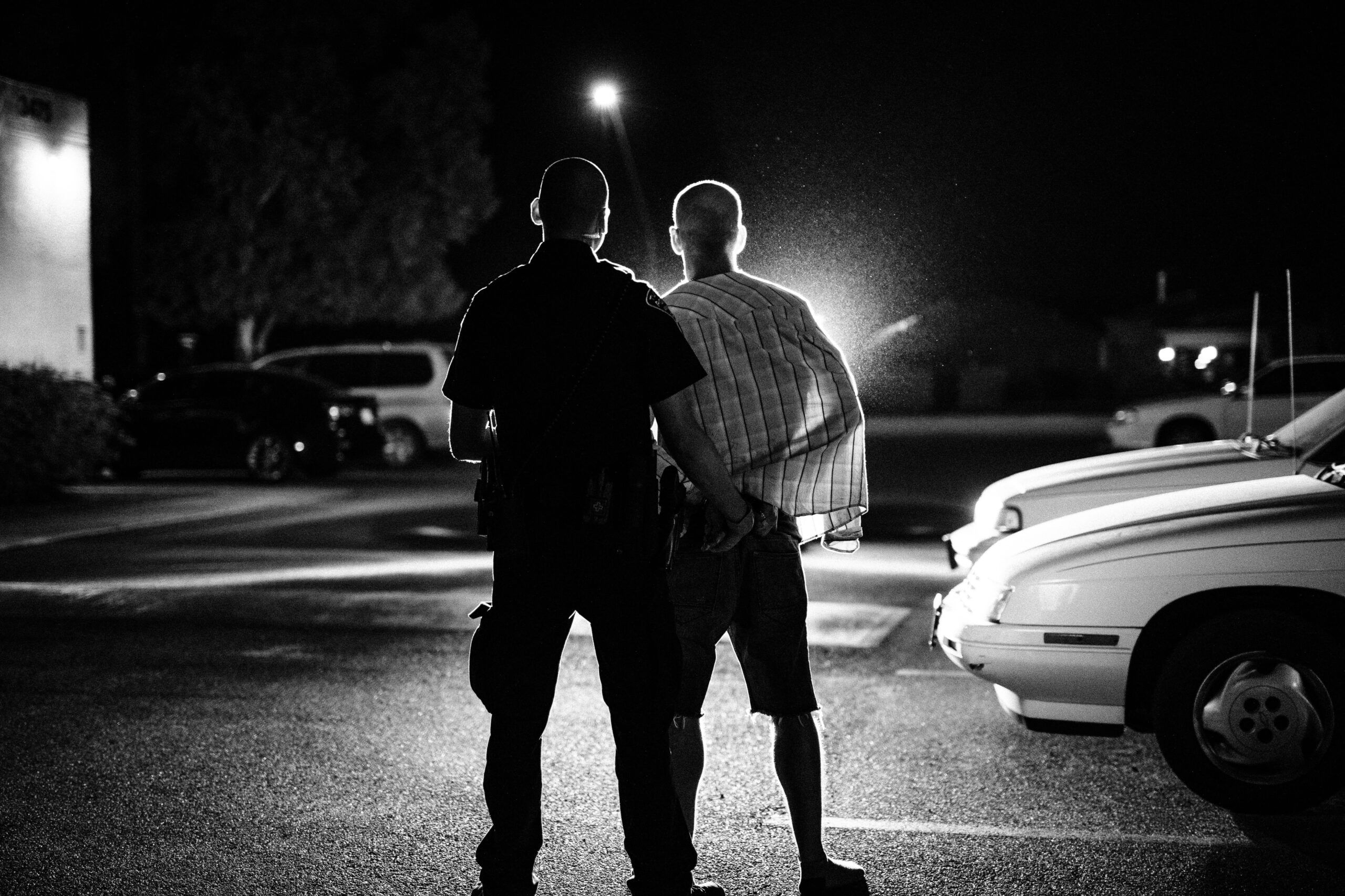 An officer with a handcuffed subject in a spotlight